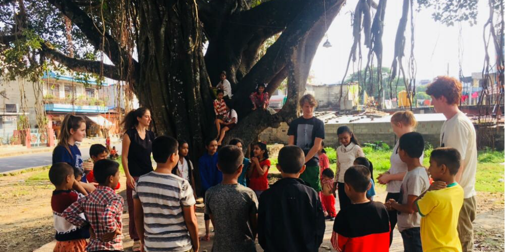 Childrn din Pokhara se adună sub un copac mare cu voluntari din GVI.